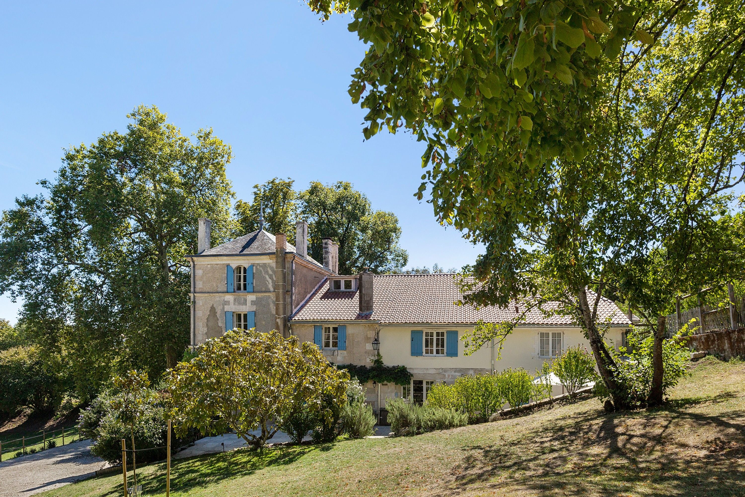 Une maison à deux étages, avec un toit en tuiles, entourée d’arbres et d’une pelouse.