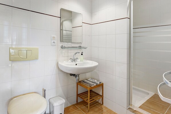 A bathroom with a white sink, a mirror, a toilet, and a shower area.