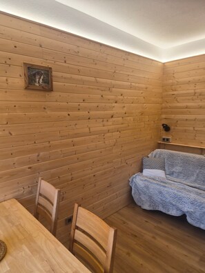 Ein Holzblockhaus-Innenraum mit Esstisch, Stühlen, einer Couch und einem gerahmten Bild an der Wand.