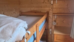 En säng med våningssäng i trä, med en undre våningssäng, en byrå i trä med lådor och en liten hylla med en karta.