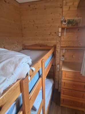 Ein hölzernes Etagenbett mit unterem Bett, eine Holzkommode mit Schubladen und ein kleines Regal mit einer Karte.
