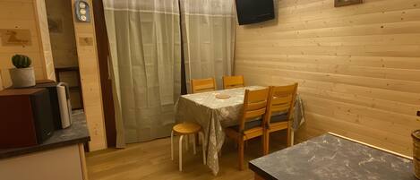 Une cuisine compacte avec des meubles en bois, une table à manger avec des chaises, un petit réfrigérateur et un téléviseur à écran plat fixé au mur.