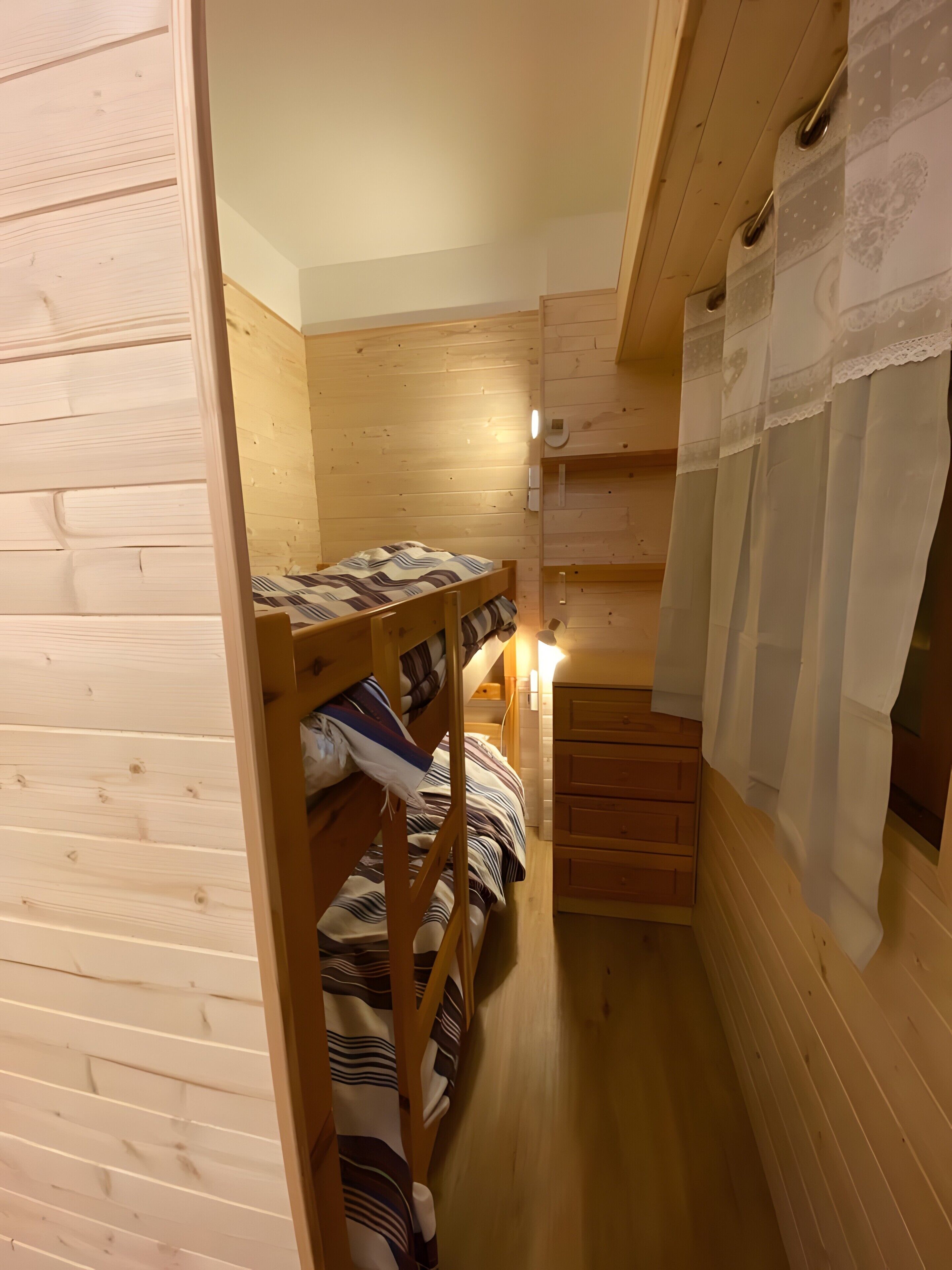 A wooden bunk bed room with a small desk and a window with curtains.