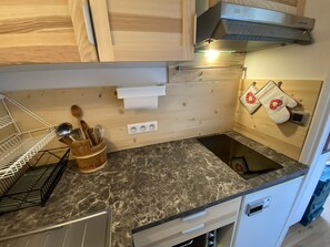 A kitchen with wooden cabinets, a marble countertop, a built-in oven, and a hanging pot rack. - Studio “La Cachette De Marmotte & Myrtille” with Mountain View and Balcony (Fontcouverte-la-Toussuire)