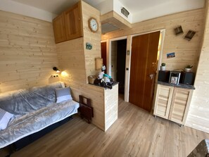 Une pièce de taille modeste comprenant un canapé, une armoire en bois, une horloge et un petit coin cuisine.