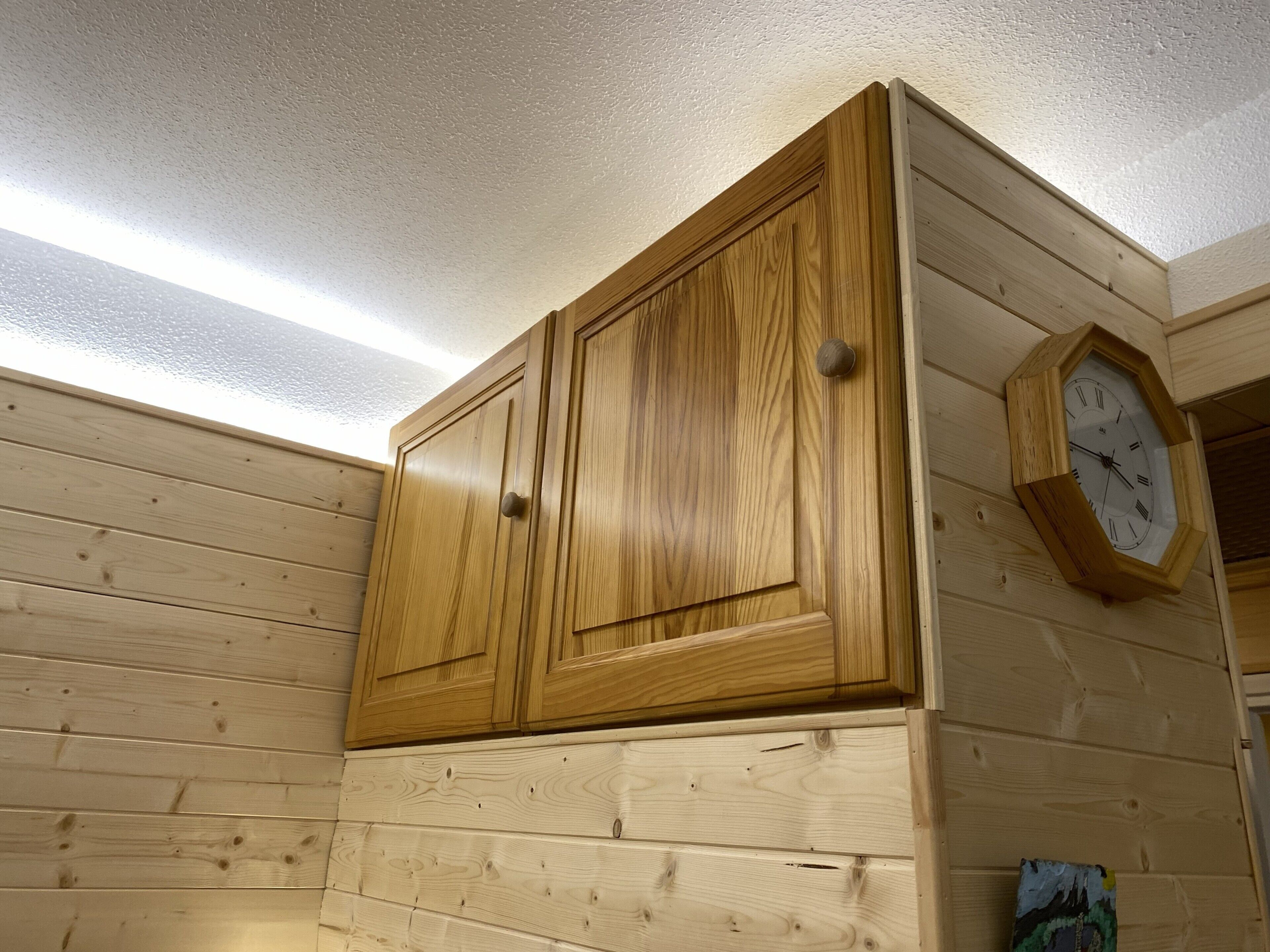 A wooden cabin interior with a wooden wardrobe and a wall-mounted clock.