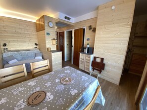 A cozy room with a bed, a dining table, and a kitchenette.