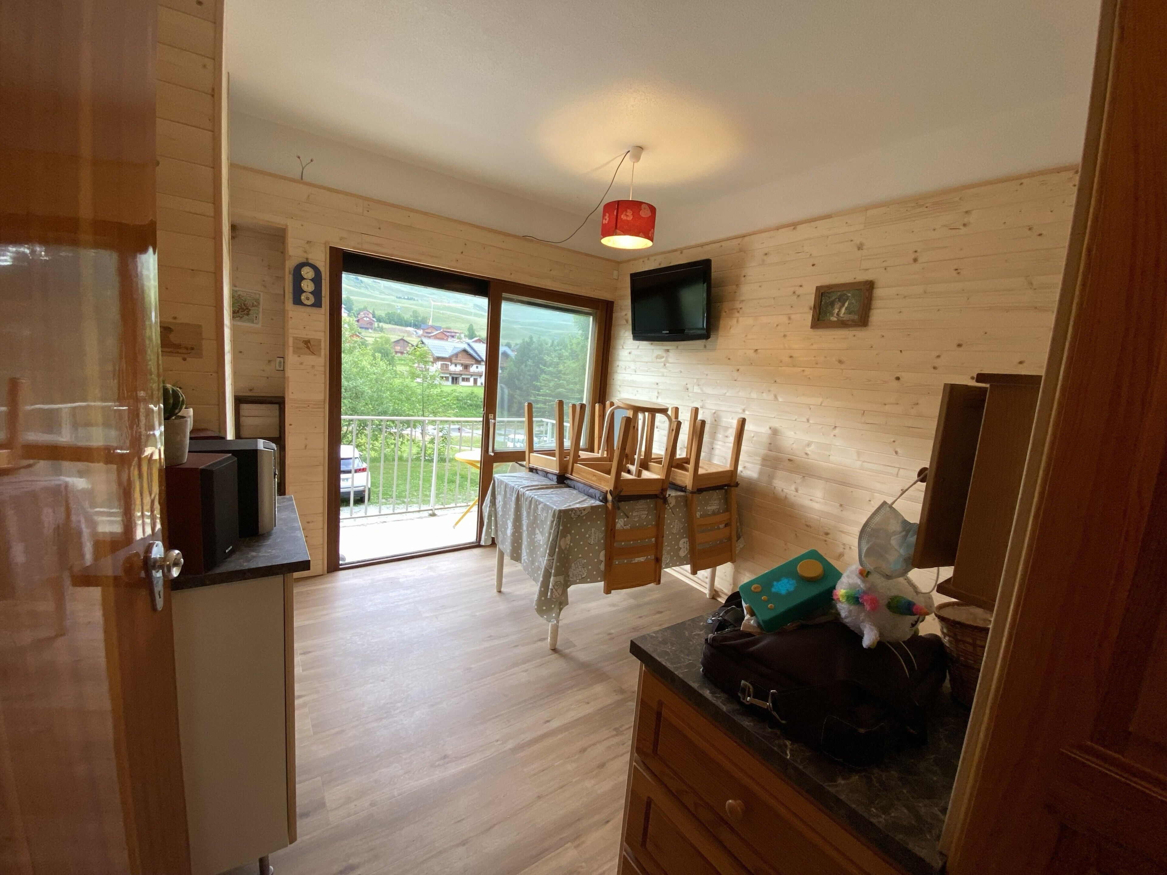 Ein Zimmer mit Holzvertäfelung, einem Esstisch mit Stühlen, einem an der Wand befestigten Fernseher und Blick ins Freie durch eine Glastür.
