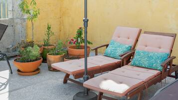 A patio with two cushioned lounge chairs, a metal umbrella, and various potted plants.