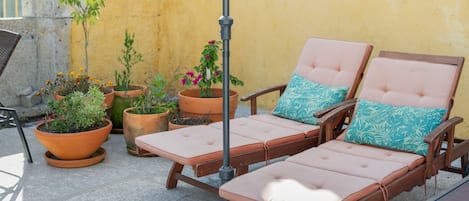 A patio with two cushioned lounge chairs, a metal umbrella, and various potted plants.