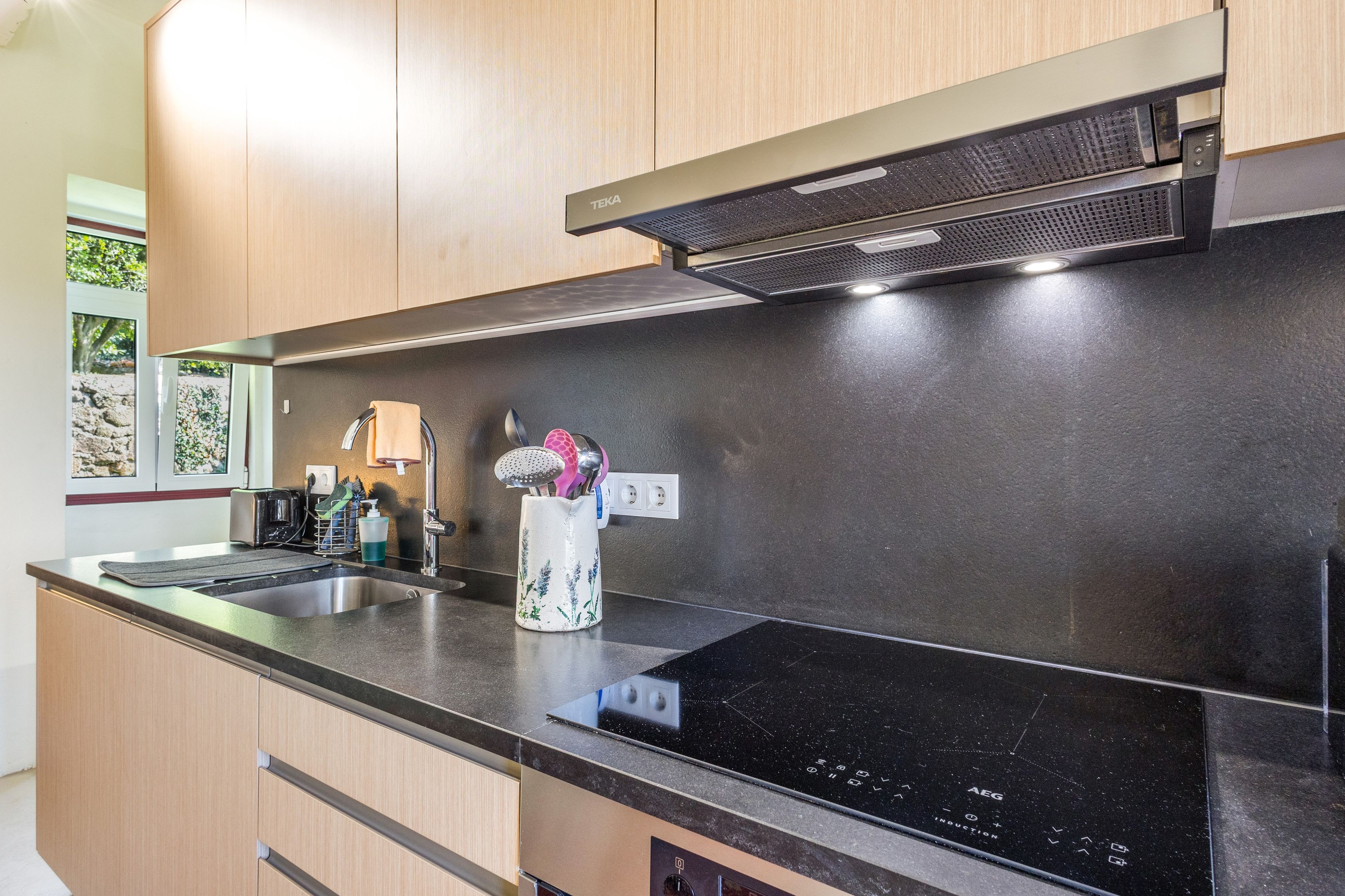 A modern kitchen with a black induction cooktop, wooden cabinets, and a stainless steel sink.