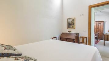 A bedroom with a bed, a wooden chest of drawers, a small table with a vase, and a framed picture on the wall.