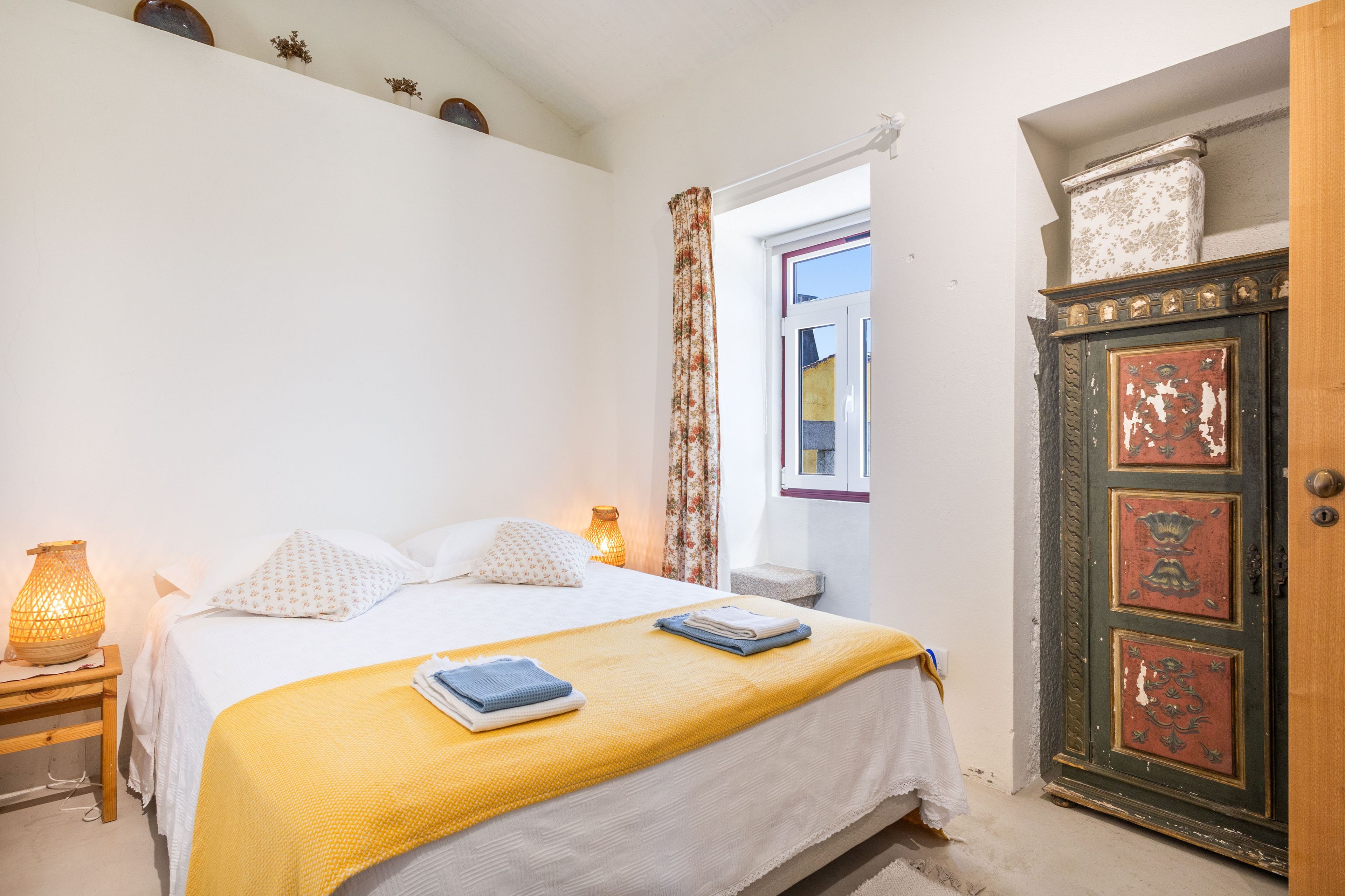 A bedroom with a bed, a nightstand, a lamp, a window with curtains, and a door with decorative panels.