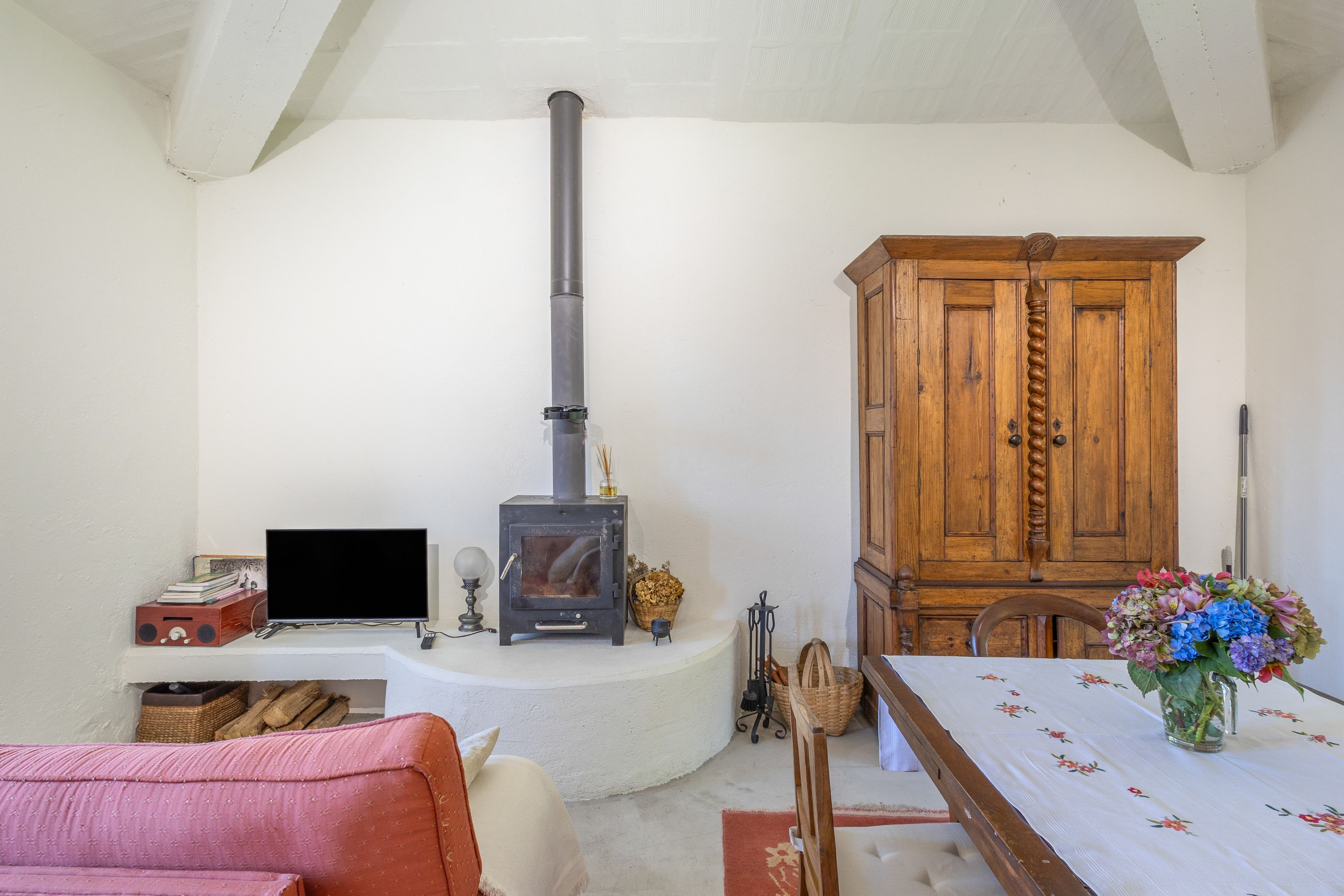 A living room with a fireplace, a television, a cabinet, and a dining table with a vase of flowers.
