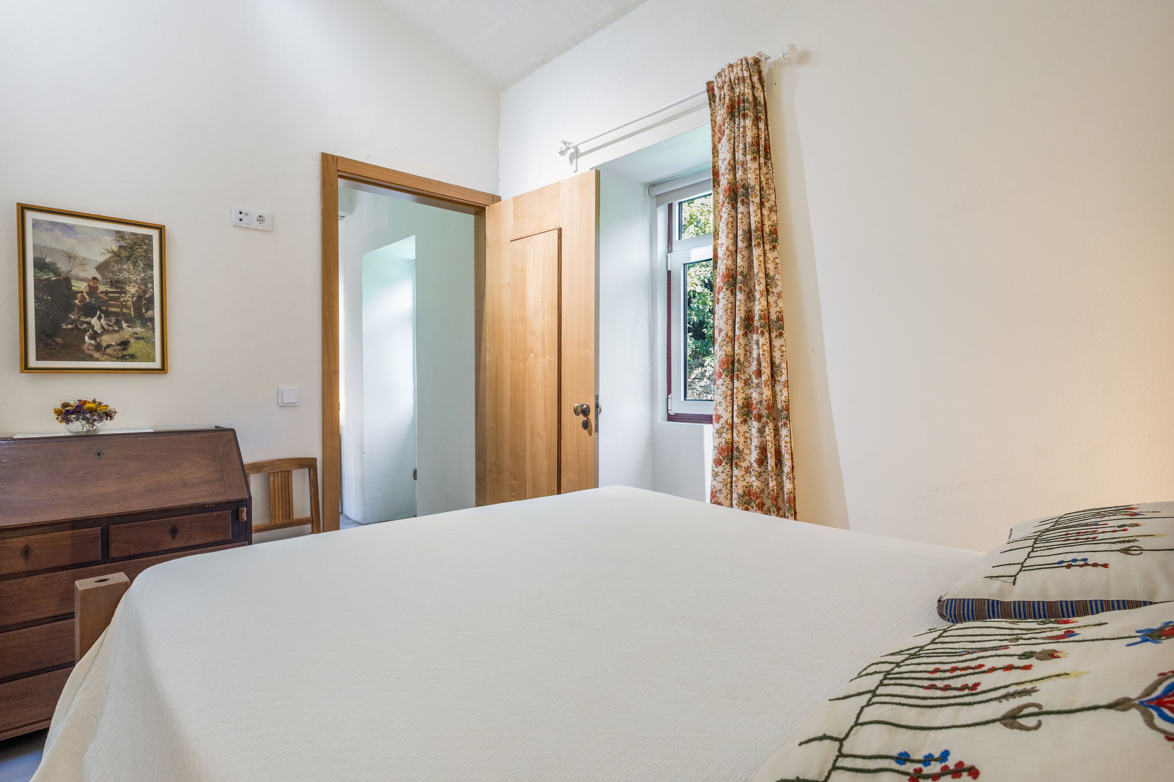 A bedroom with a bed, a dresser, a door, and a window with curtains.