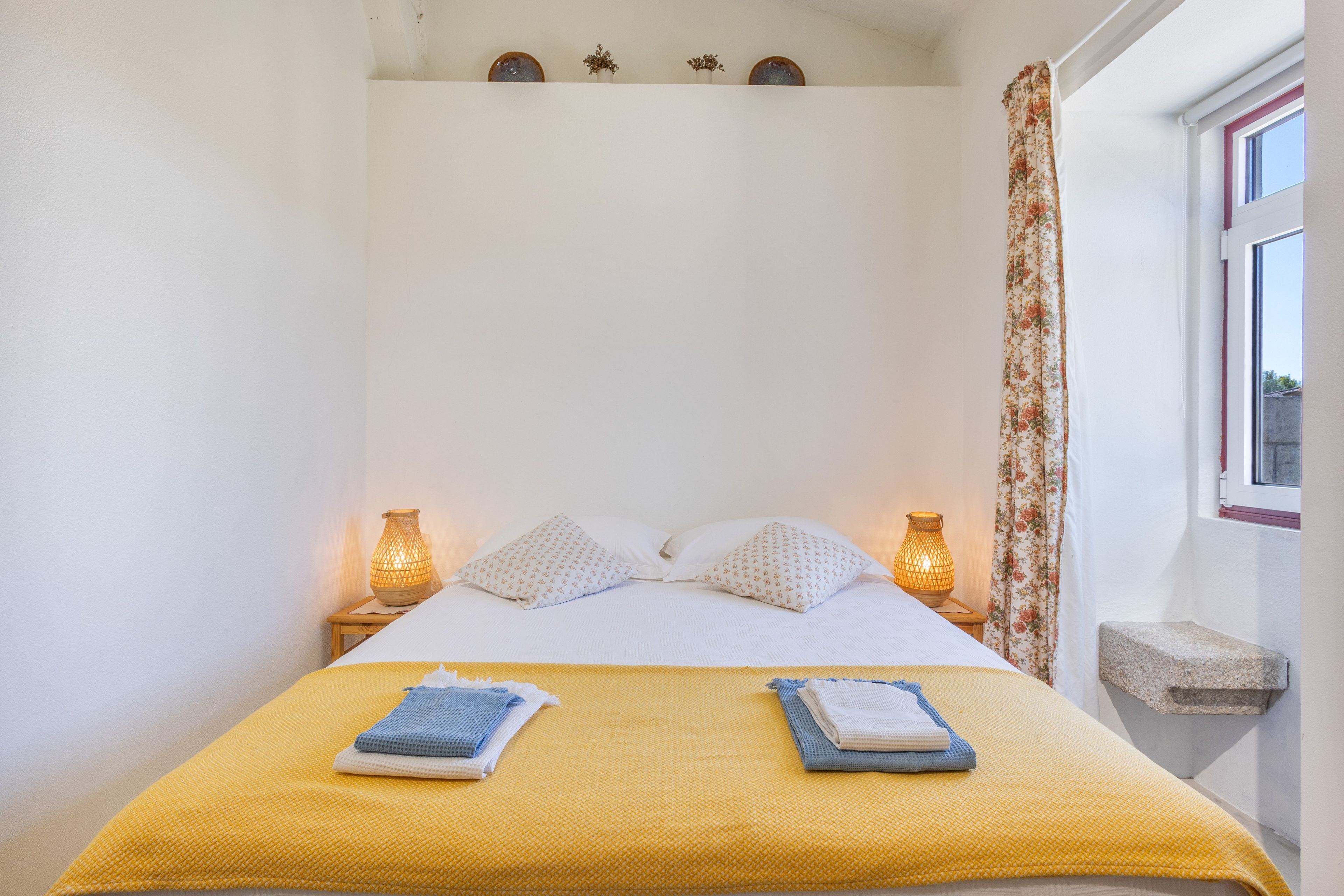 A bed with two pillows, a yellow blanket, and two folded towels on a white bedspread.