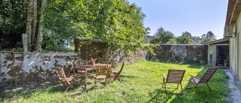 A rustic outdoor seating area with a stone wall, wooden furniture, and lush greenery.