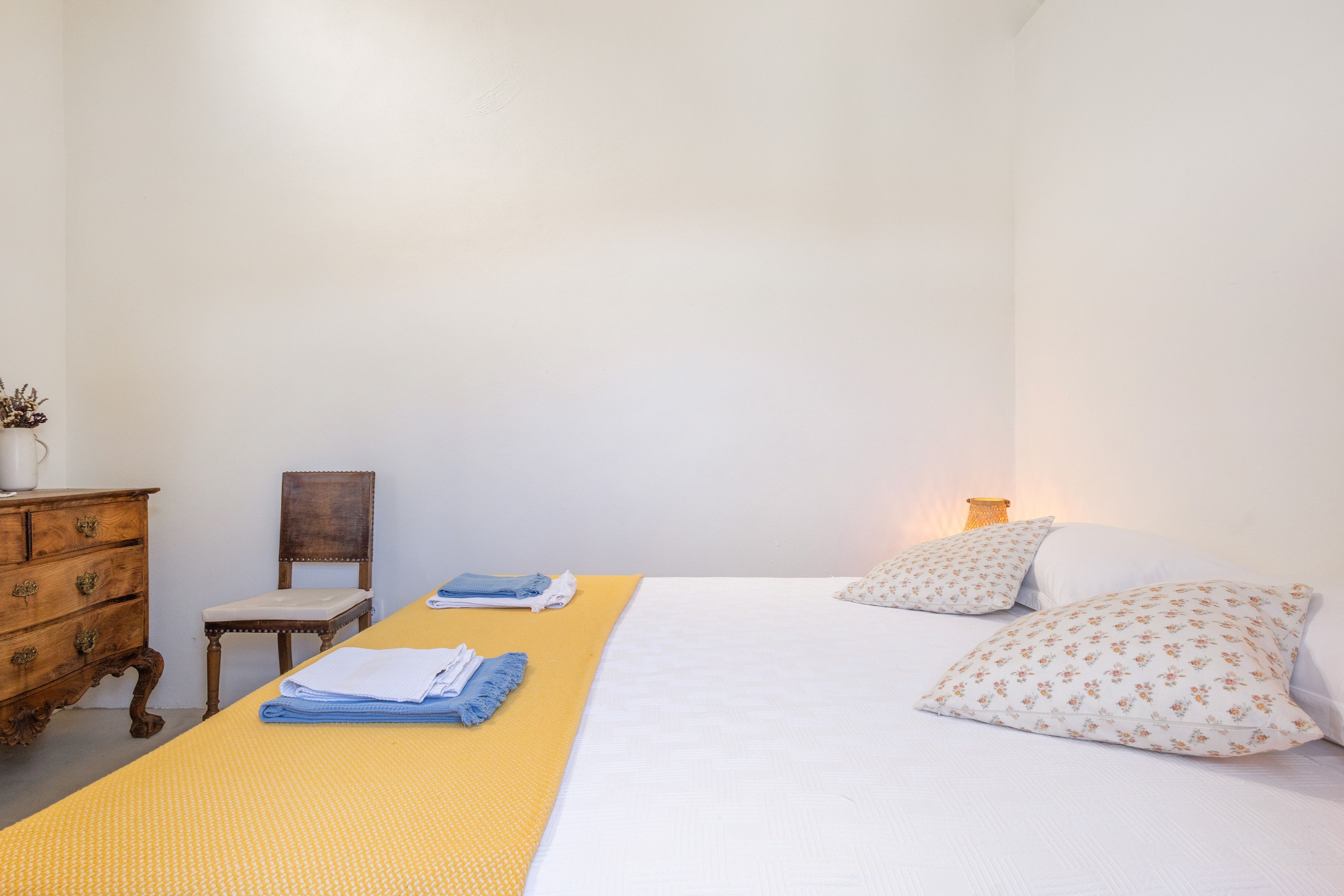 Une chambre à coucher avec un lit, une commode en bois, une chaise et une table sur laquelle sont pliées des serviettes.