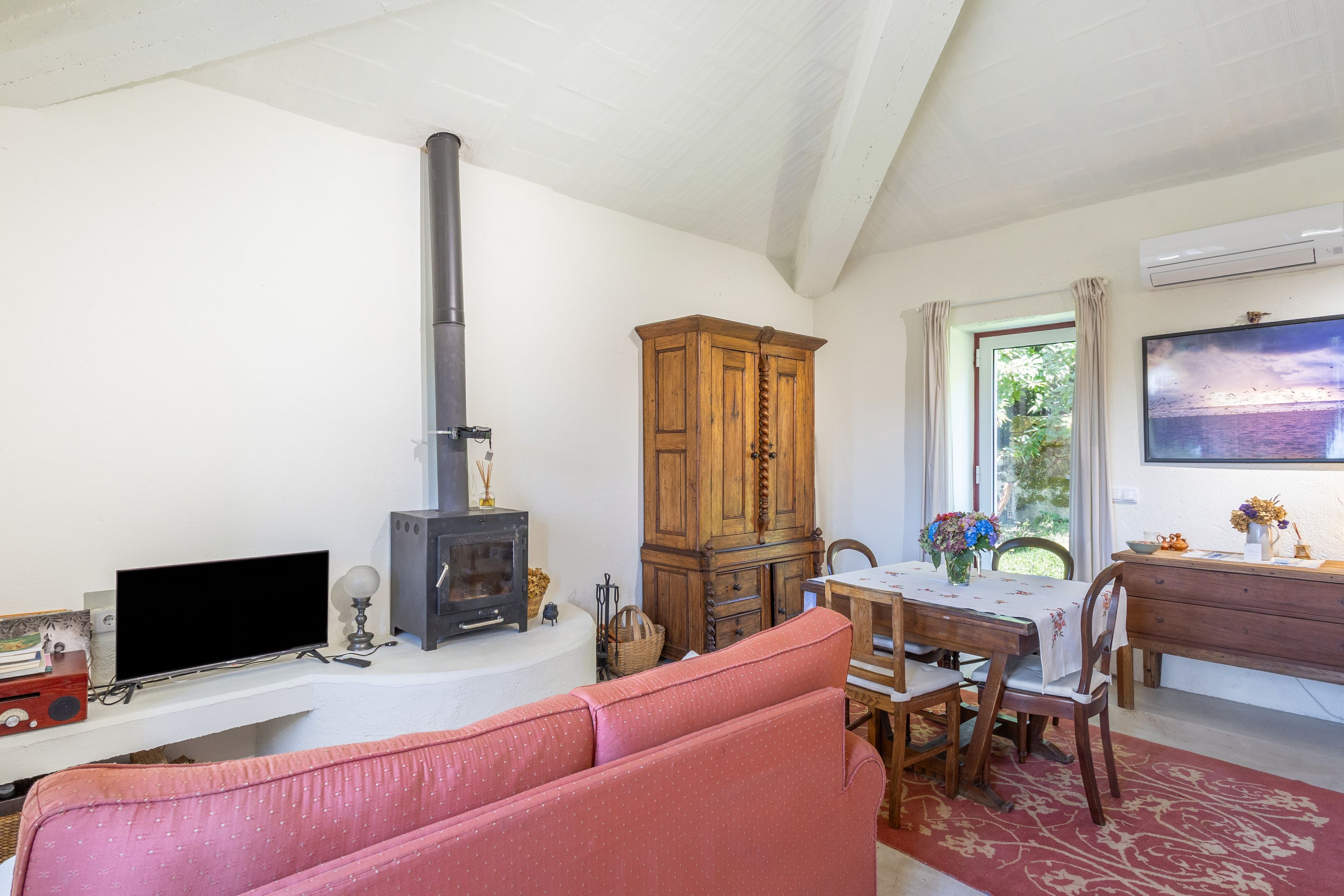 A living room with a fireplace, a television, a sofa, a dining table with chairs, and a window with a view.