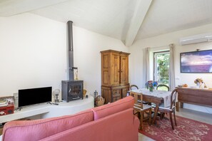 A living room with a fireplace, a television, a sofa, a dining table with chairs, and a window with a view. - Casa do Caseiro: Mountain View, Wi-Fi & Air Conditioning (Sandiães)