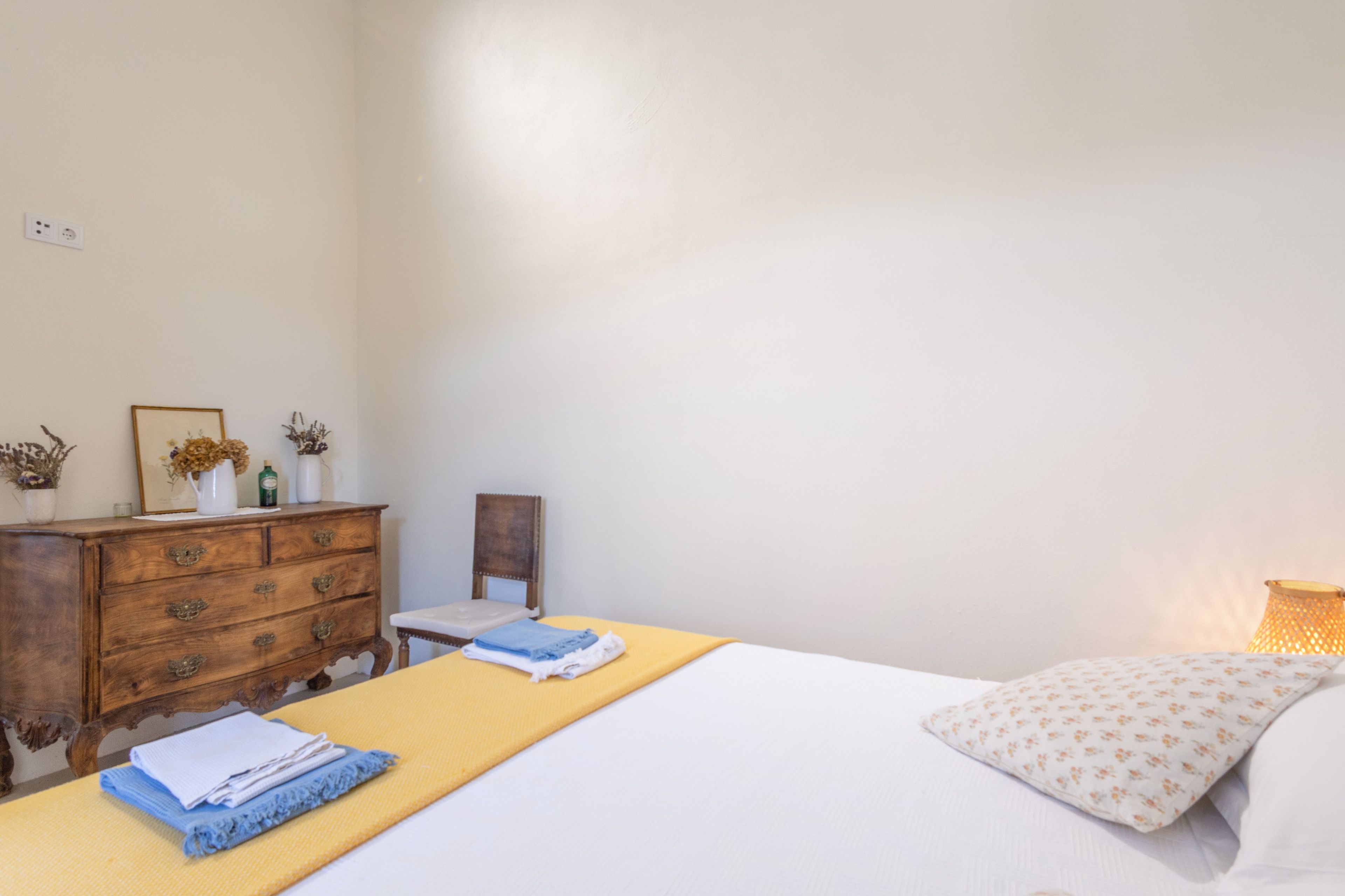 A bedroom with a bed, a wooden dresser, a chair, and a bedside table.