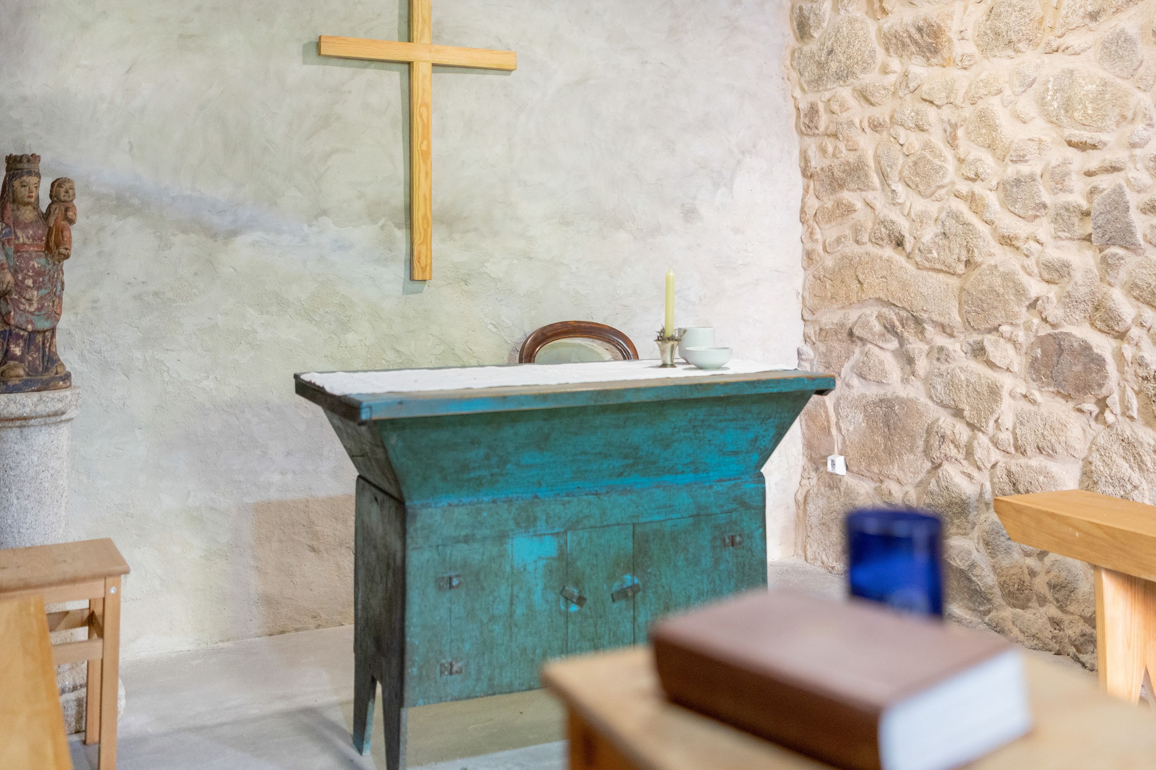 A church interior with a wooden altar, stone wall, and a statue.