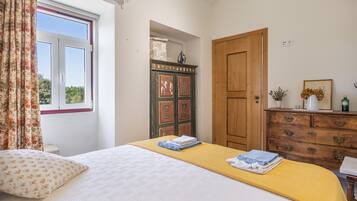 A bedroom with a bed, a wooden wardrobe, a dresser, and a window with curtains.