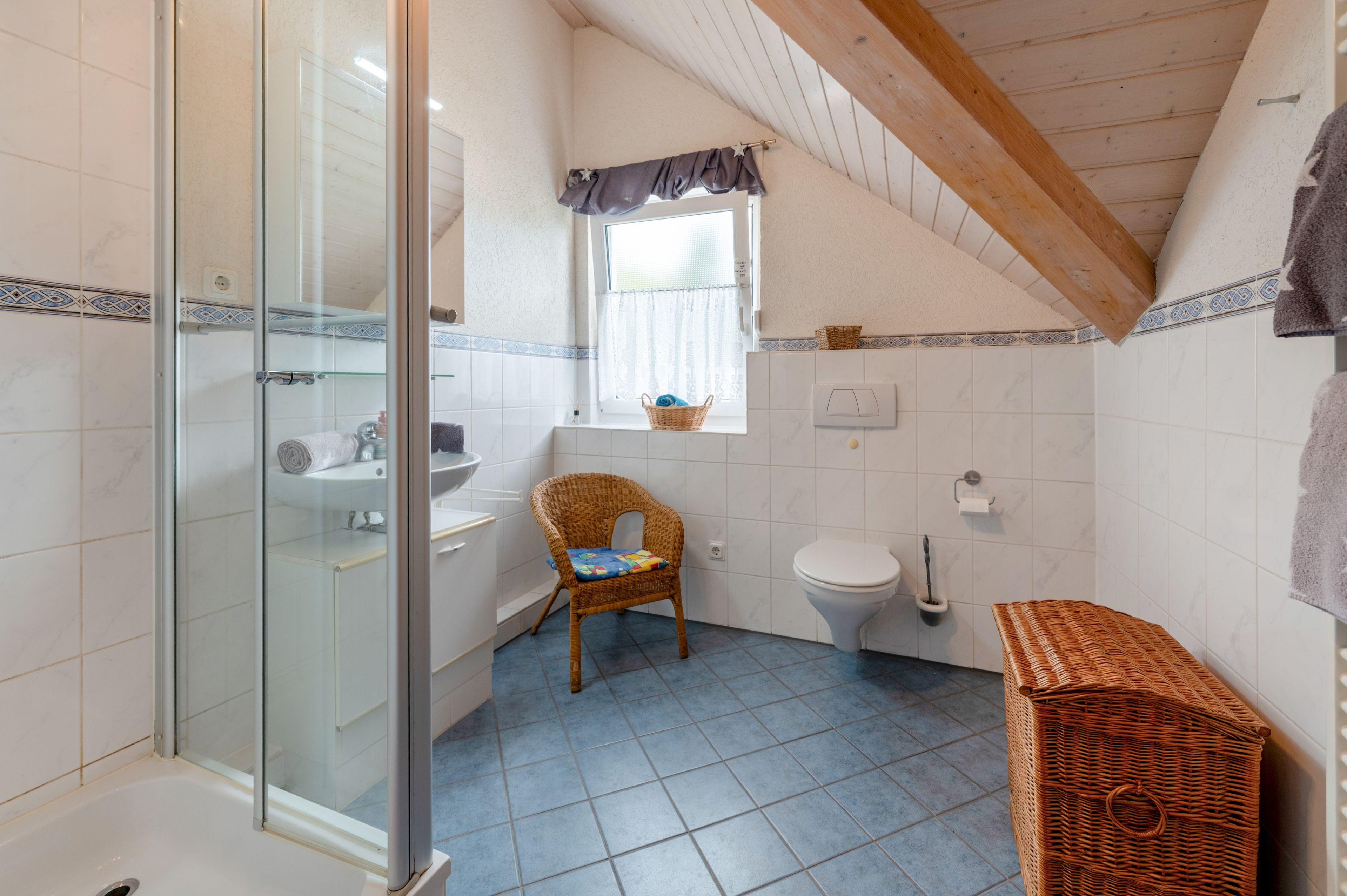 Ein Badezimmer mit Duschkabine aus Glas, einem weißen Waschbecken, einer Toilette und einem Korbstuhl.