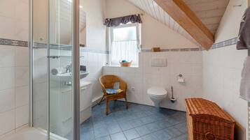 A bathroom with a glass shower enclosure, a white sink, a toilet, and a wicker chair.