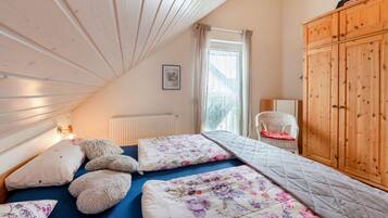 A bedroom with a sloped ceiling, a bed with floral bedding, a white chair, and wooden furniture.