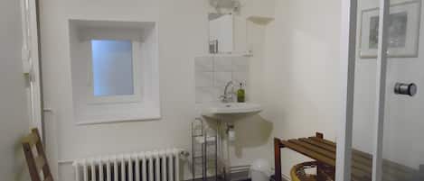Un baño con lavamanos blanco, un espejo, una ventana, un radiador y una silla de madera.