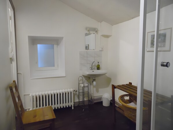 A bathroom with a white sink, a mirror, a window, a radiator, and a wooden chair.