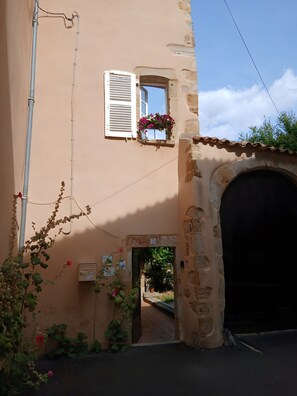 A building with a stone archway entrance, a window with shutters, and a flower box on the wall.