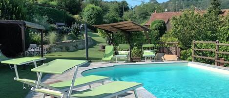 A swimming pool with green lounge chairs and a pergola.