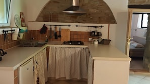 A kitchen with a gas stove, hanging utensils, and a brick wall.