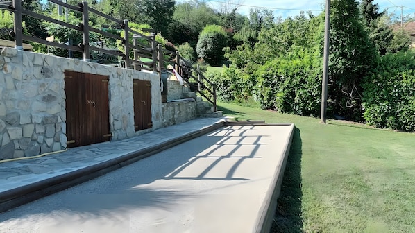 A stone wall with wooden doors, a paved area, and a grassy lawn.