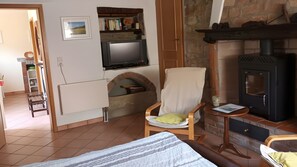 Una sala de estar con chimenea, un televisor montado en la pared, un sillón cómodo y una cama con manta a rayas.