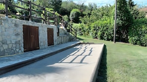 A stone wall with wooden doors, a concrete pathway, and a grassy area with trees.
