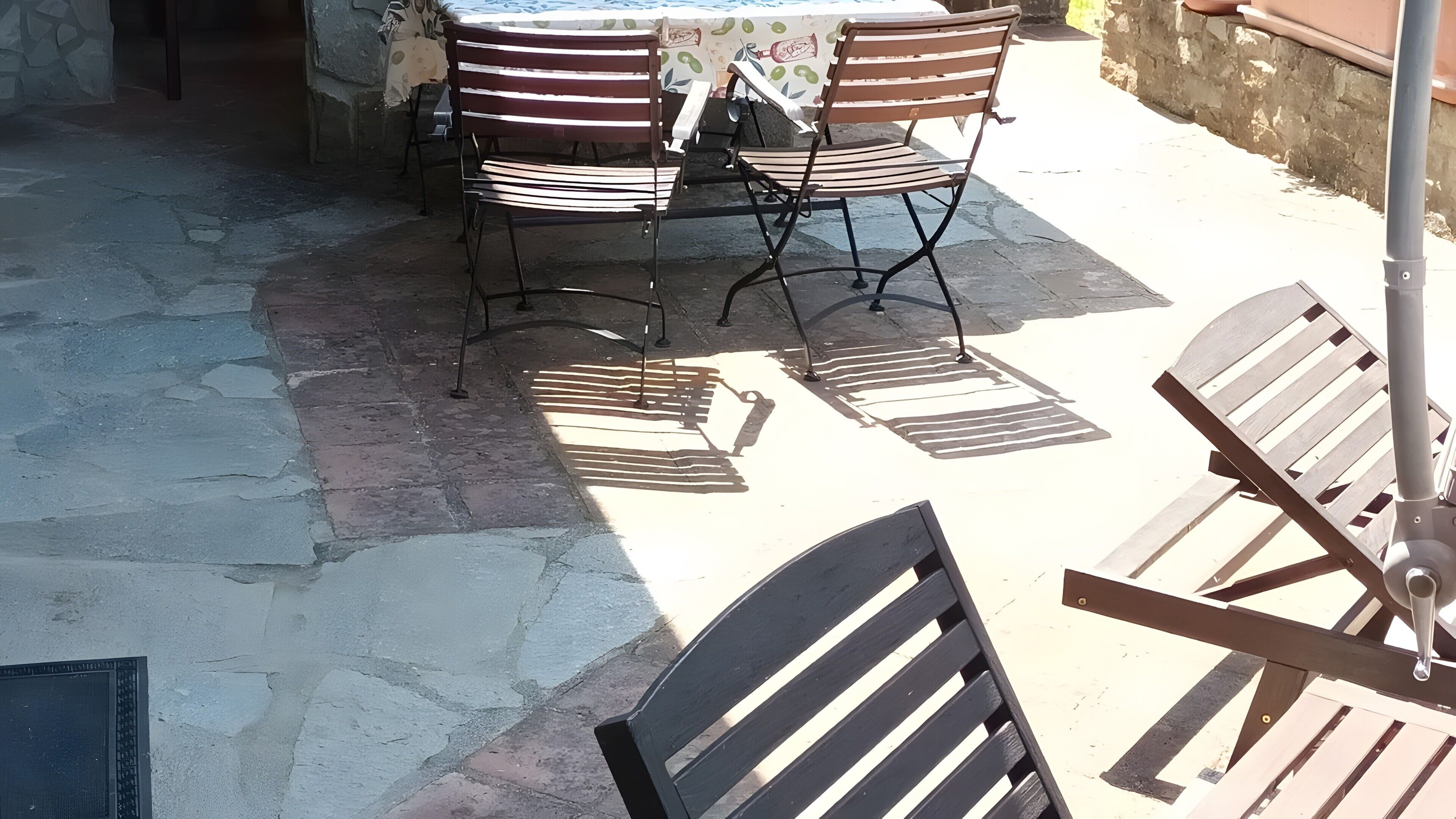 Un espace patio avec une table et des chaises, un sol en pierre et un mur orné d’un motif de fruits.