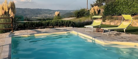 A swimming pool with two lounge chairs and a view of the countryside.