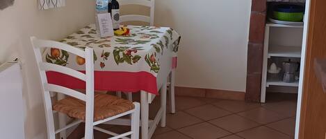 Een eetgedeelte met een tafel bedekt met een bloemendecoratie, twee stoelen, een waterfles, een fles olijfolie en een fruitschaal.