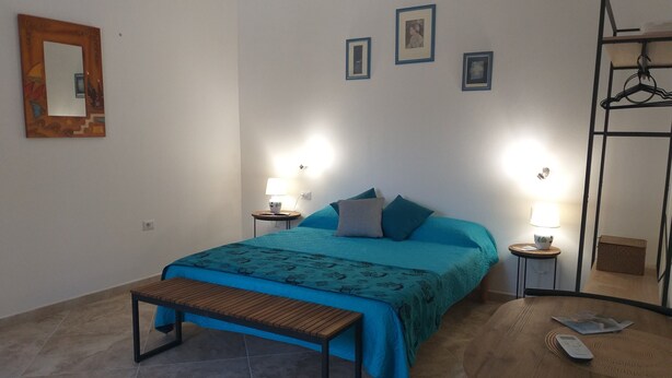 Un dormitorio con cama, mesitas de noche, un banco, una mesa redonda y un armario.