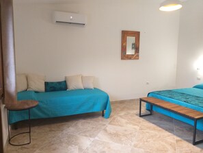 A room with two beds, a small table, an air conditioning unit, and a mirror on the wall.