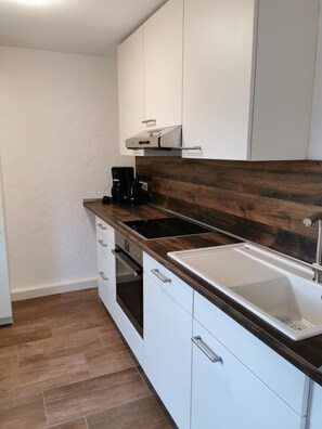 Una cocina compacta con armarios blancos, encimera de madera oscura, horno empotrado y un lavamanos.