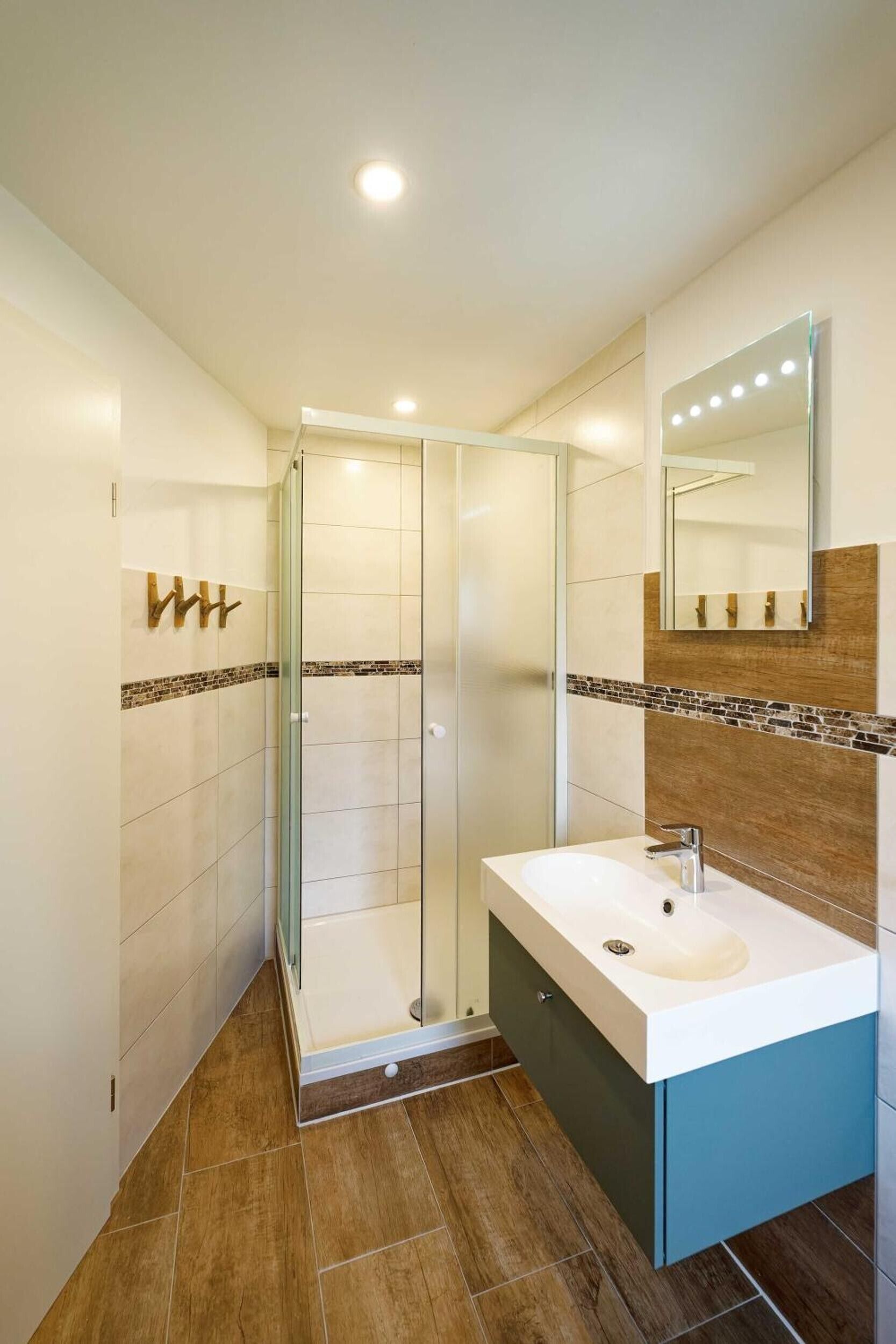 A modern bathroom with a glass shower enclosure, a vanity with a sink, and a mirror with lights.