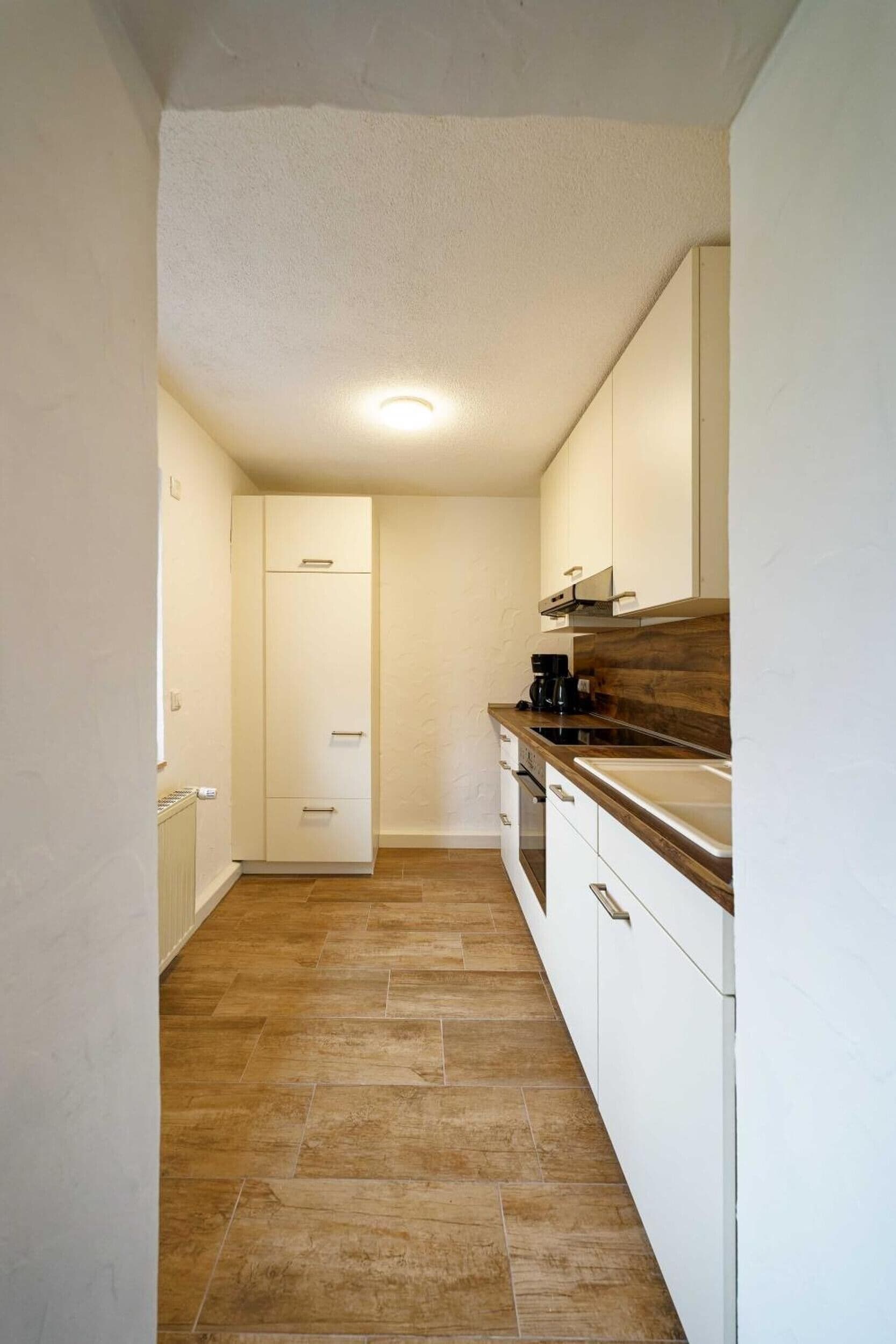 Une cuisine étroite avec des meubles blancs, un plan de travail en bois et un sol carrelé.