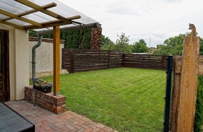 A backyard with a wooden fence, a pergola, and a brick planter with flowers.