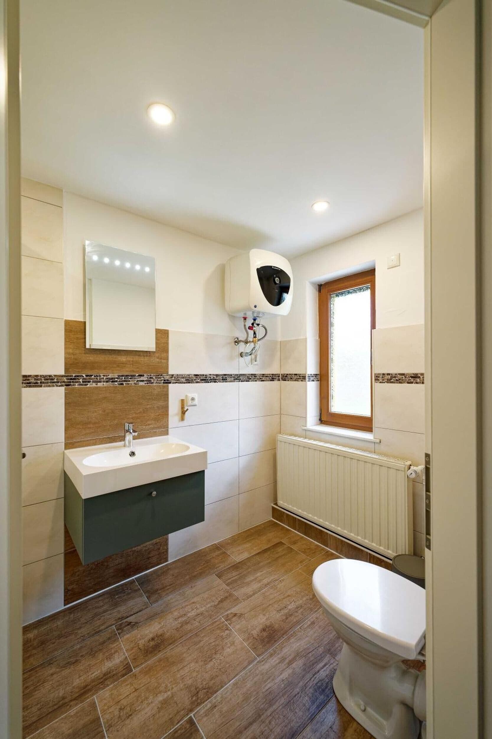Ein Badezimmer mit weißem Waschbecken, einem Spiegel, einer Toilette und einem Fenster.