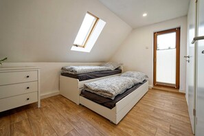 A small, single-room apartment with a sloped ceiling, a skylight, a wooden floor, a white dresser, and a door with blinds.