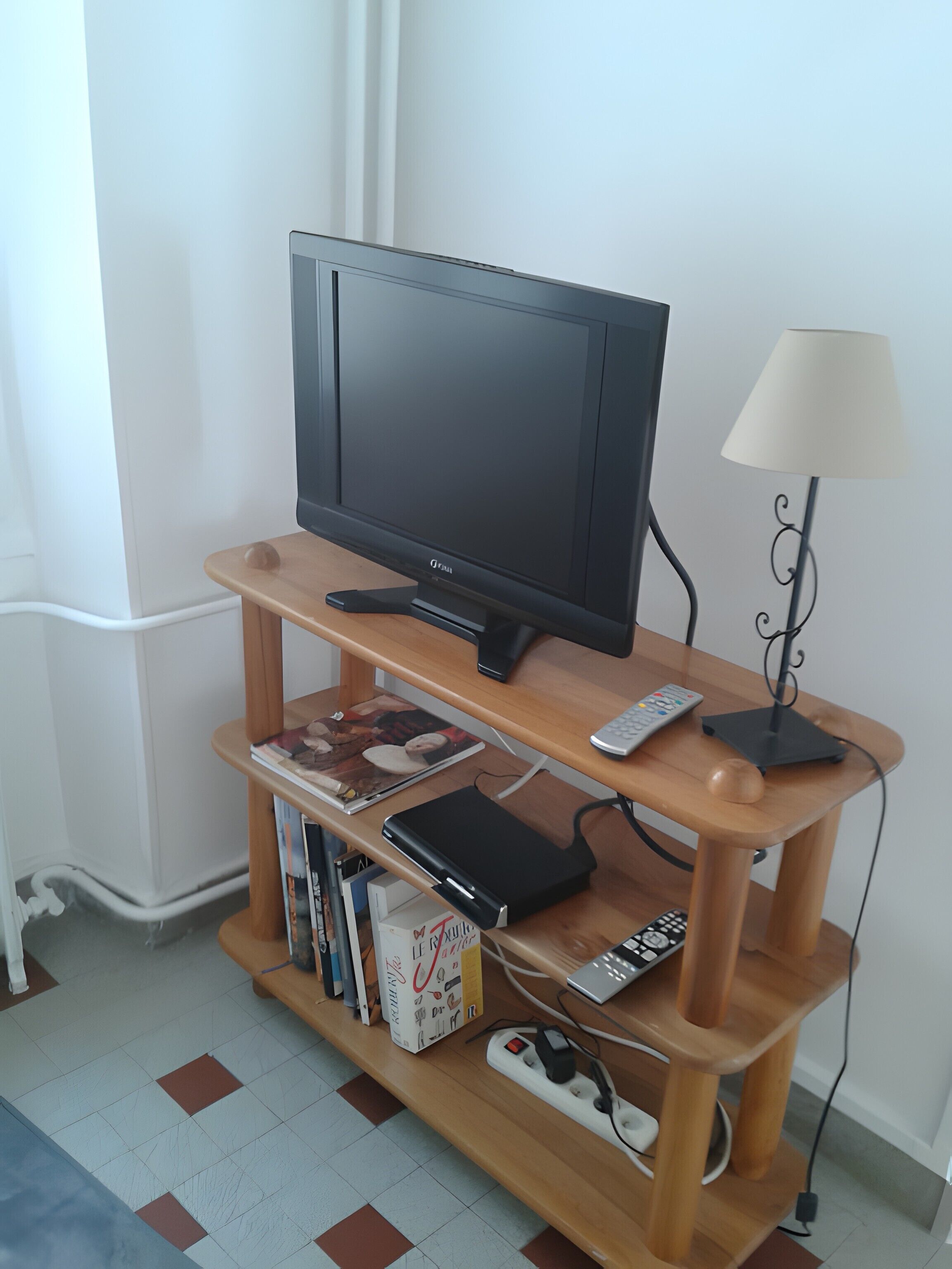 Een televisie op een houten standaard, met afstandsbediening, boeken en een stekkerdoos.